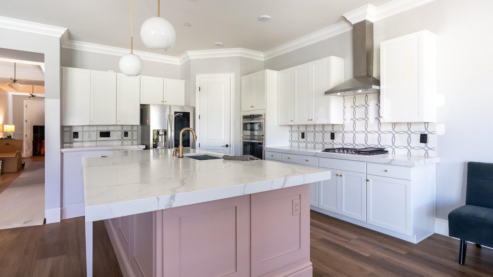 White shaker kitchen with a blush painted island under a white marble-look quartz top, a stainless chimney hood and glass globe pendants