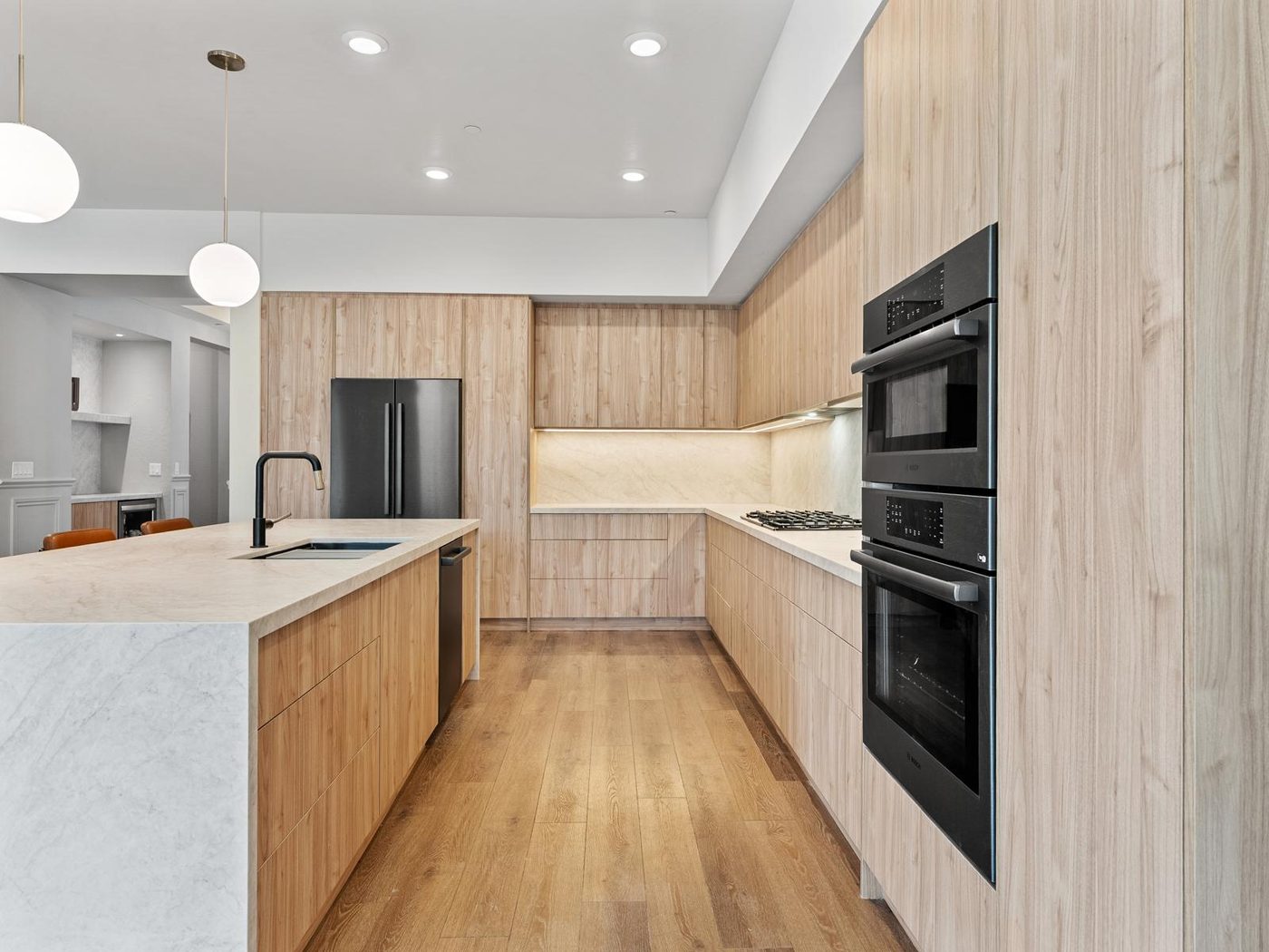 Light oak kitchen with quartz countertops, a wall oven stack and an island sink